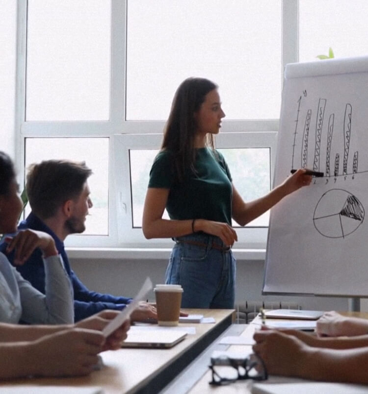 Presentation giving by a woman on white board while a group of executives listening