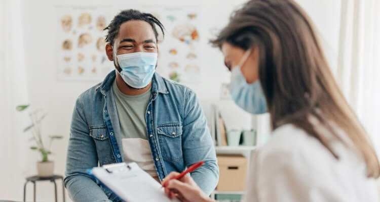 A lady doctor writing prescription for a male smiling patient , but wearing masks